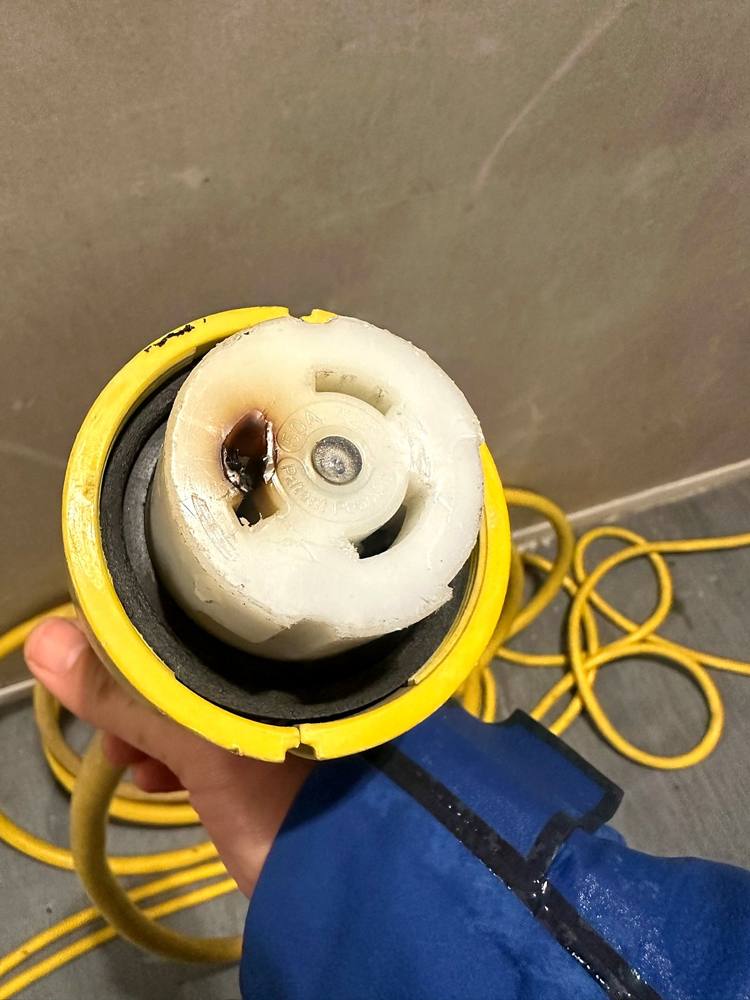 A shore cord's boat-end plug with brown burn marks and melted plastic around one pin