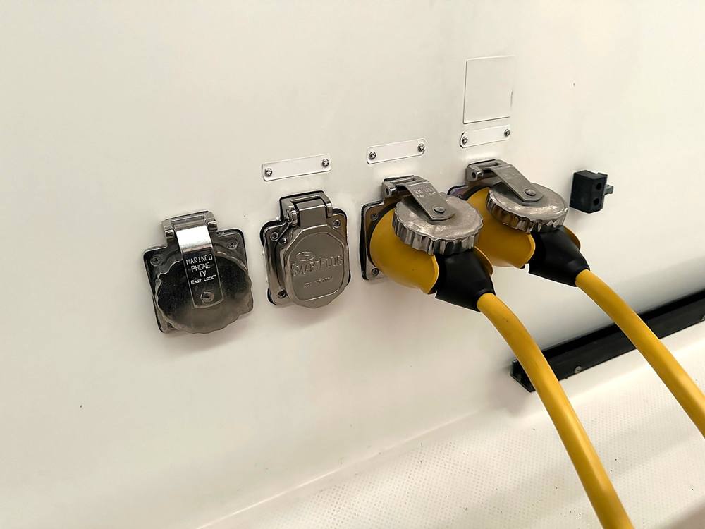 Two stainless shore inlets on a white hull with yellow cords locked in, each with a label plate above it