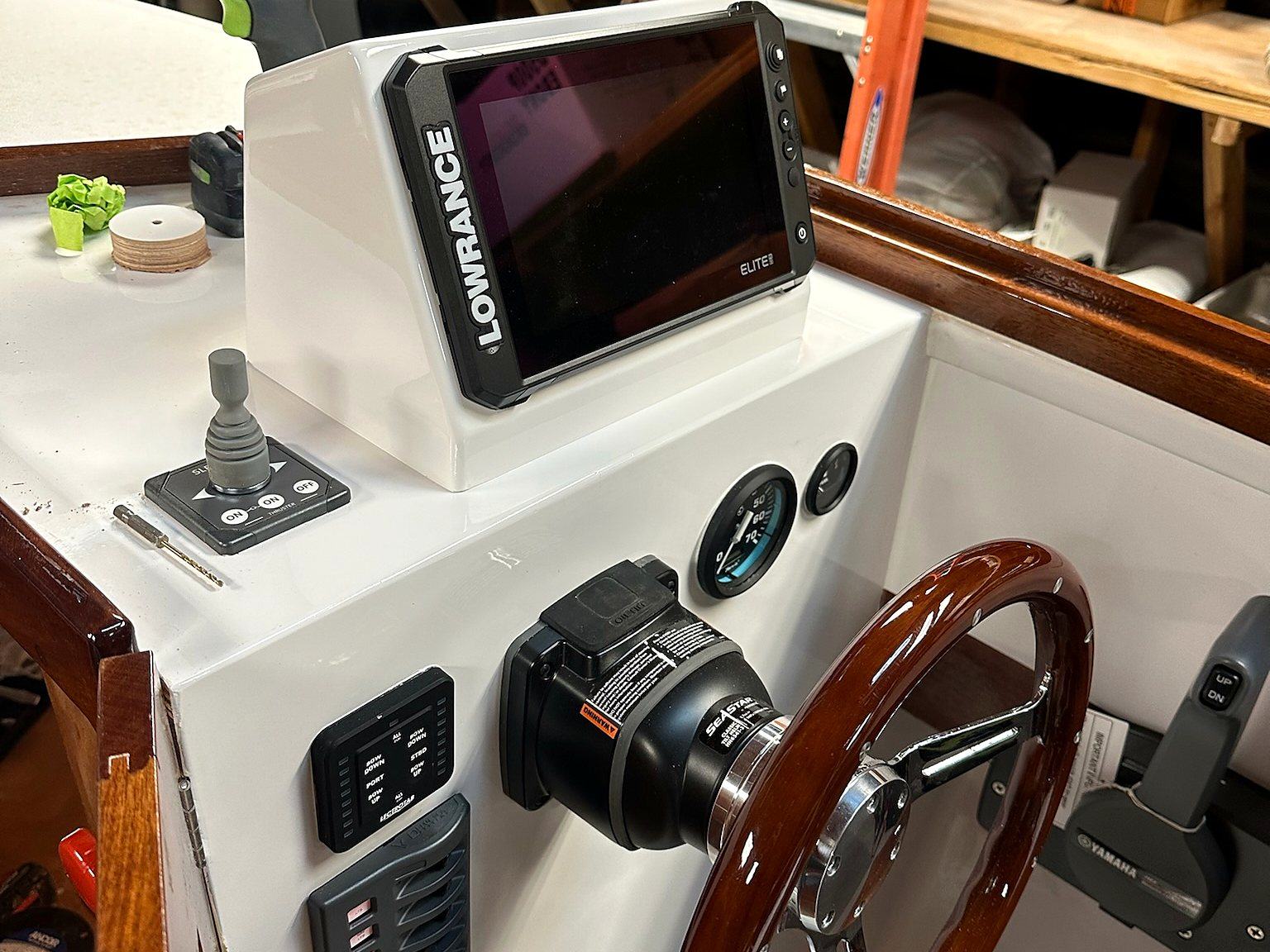 A finished helm console with a chartplotter, switch panels and a wood steering wheel