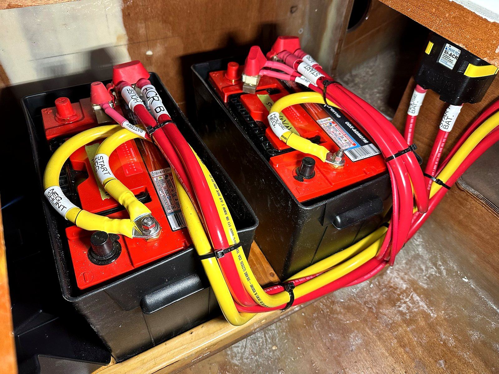 Two batteries in their boxes with red positive and yellow negative cables, every cable labelled, and an automatic charging relay on the bulkhead
